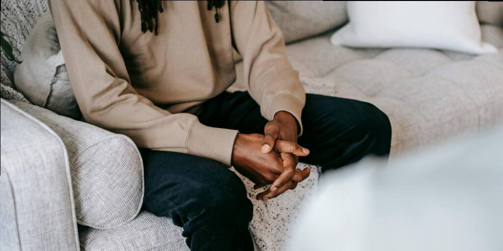 Man sits on counselling sofa with his hands linked together